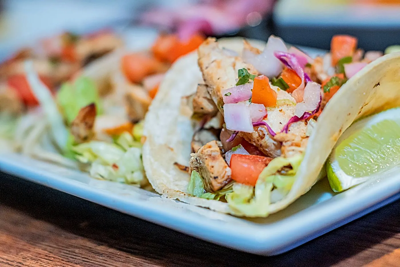 A close-up of grilled pollo (chicken) street tacos with pico de gallo, red onion and lime
